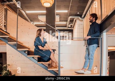Businesswoman sitting on steps and talking with businessman in office Stock Photo