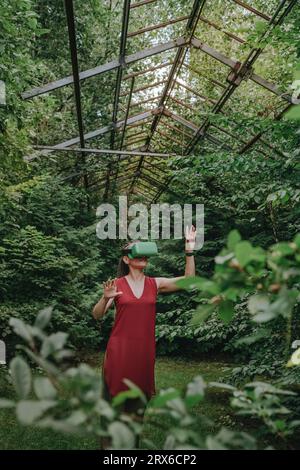 Woman wearing VR headset and gesturing in greenhouse Stock Photo