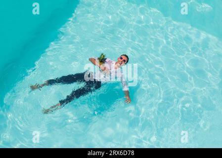 Happy man swimming with pineapple in pool Stock Photo