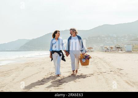 Happy man holding basket and walking with woman at beach Stock Photo