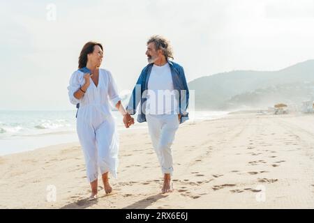 Happy senior couple holding hands and walking at beach Stock Photo