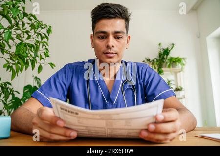 Young doctor analyzing reports at desk in clinic Stock Photo