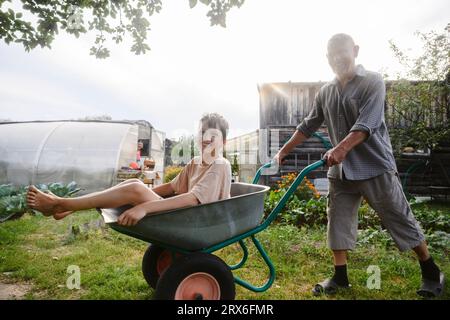 Smiling grandfather riding grandson on wheelbarrow Stock Photo