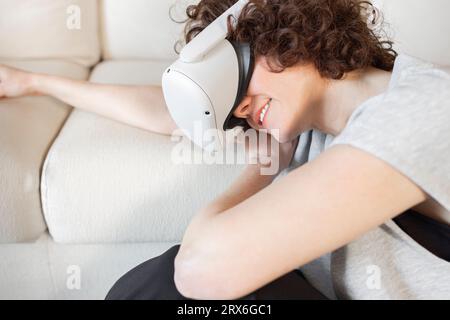 Smiling woman wearing virtual reality headset resting on sofa at home Stock Photo