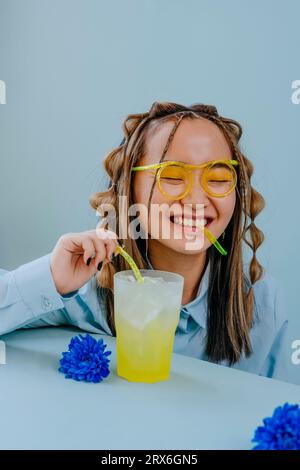 Happy woman drinking juice through glass-like straw in studio Stock Photo