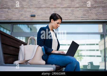 Focused businesswoman using laptop and sitting on bench Stock Photo