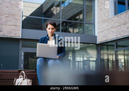 Businesswoman using laptop and sitting on bench Stock Photo