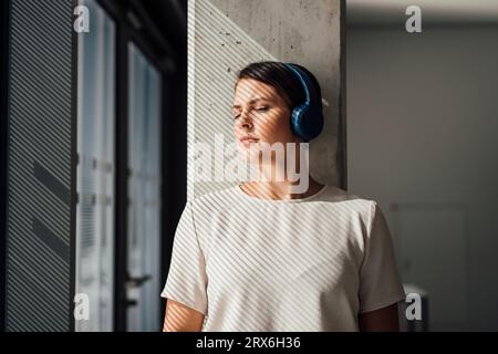 Businesswoman listening to music and leaning on column Stock Photo