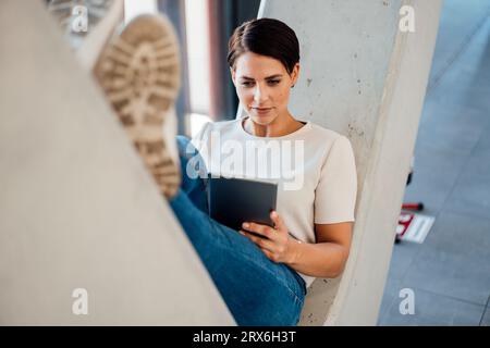 Businesswoman using tablet computer sitting on V-shaped column Stock Photo