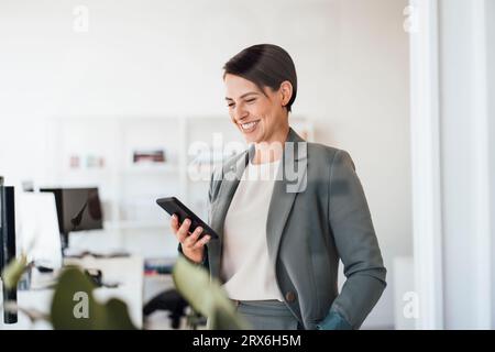 Smiling businesswoman using smart phone in office Stock Photo
