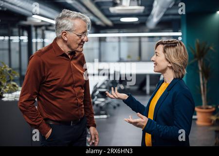 Smiling businesswoman gesturing and discussing with colleague in office Stock Photo