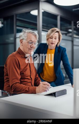 Senior businessman using tablet PC and discussing with colleague at desk in office Stock Photo