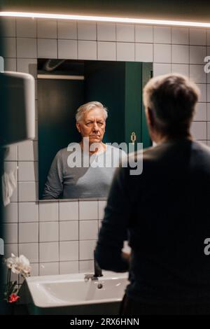 Senior man looking in mirror in bathroom Stock Photo
