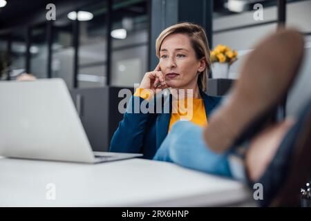Thoughtful businesswoman brainstorming over laptop at desk in office Stock Photo