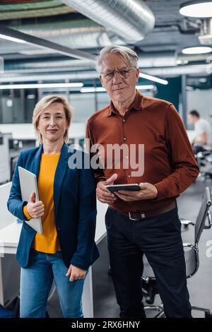Confident business colleagues with tablet PC and laptop at work place Stock Photo