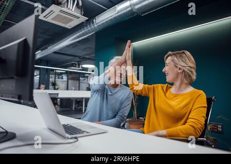 Business colleagues giving high-five to each other at desk in office Stock Photo