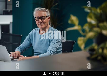 Smiling senior businessman with eyeglasses working at desk in office Stock Photo