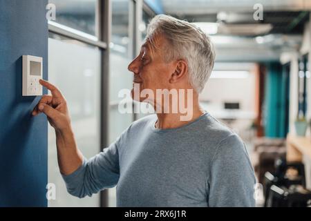 Smiling senior businessman using digital thermostat at work place Stock Photo