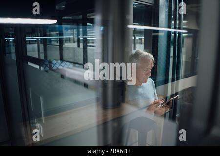 Senior businessman using mobile phone seen through glass in office Stock Photo