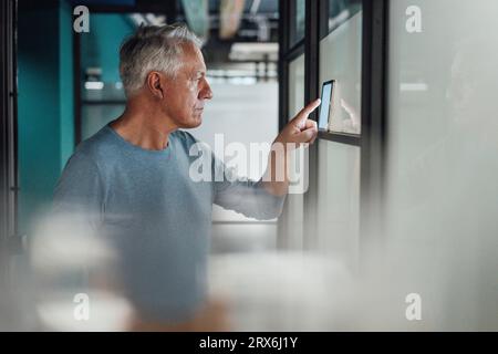 Senior businessman using tablet PC on glass wall in office Stock Photo