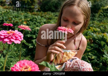 Blond girl smelling pink flower in garden Stock Photo