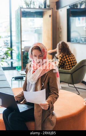 Gorgeous muslim woman in hijab working at office separately from her multiracial colleagues Stock Photo