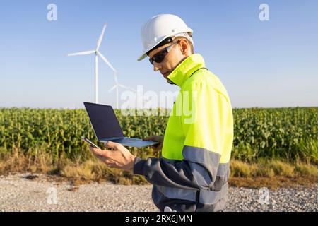 Engineer holding laptop and using smart phone on sunny day Stock Photo