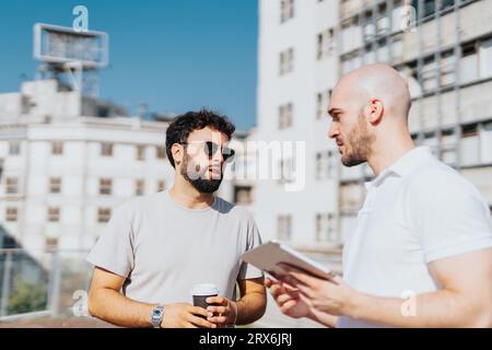 A group of architects and engineers collaborating outdoors in a city area, discussing a blueprint on a tablet and analyzing statistics. Successful tea Stock Photo