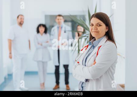 Confident female doctor in medical uniform, surrounded by happy doctors. Successful specialist providing excellent healthcare service. Stock Photo
