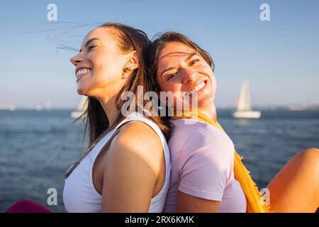 Happy friends sitting together at the waterfront Stock Photo