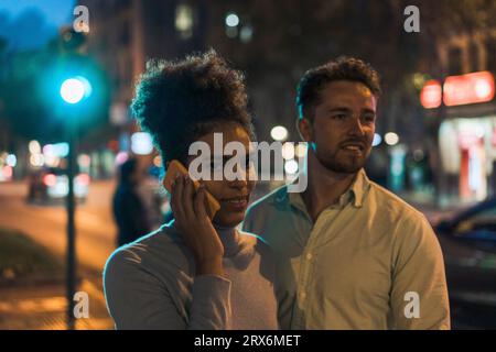 Young woman talking on smart phone with man at street Stock Photo