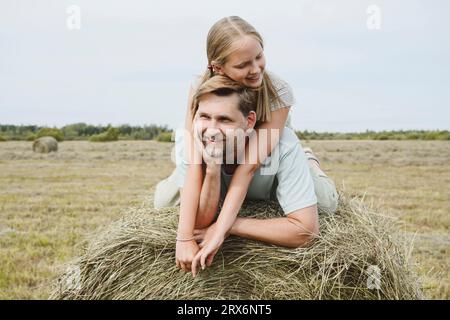 Happy daughter and father lying on hay in field Stock Photo