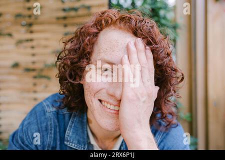 Happy redhead man covering face with hand in cafe Stock Photo
