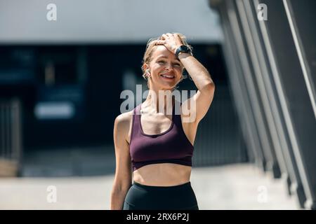 Smiling woman wearing wireless in-ear headphones standing near building Stock Photo