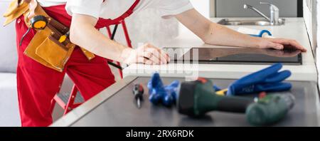 Gloved craftsman installs hob in kitchen. Household Appliance Installation Services Concept Stock Photo