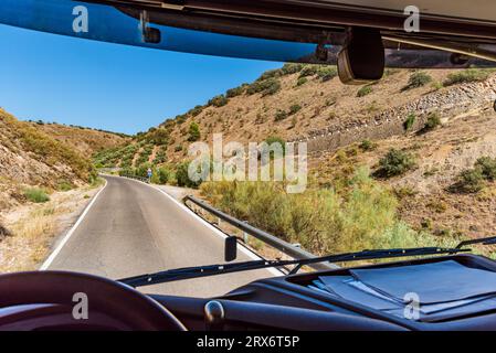 View from inside a truck of a narrow mountain road with curves and a steep slope visible. Stock Photo