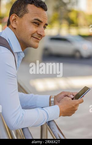 Portrait of latino man in shirt leaning on a railing using his cell phone. Stock Photo