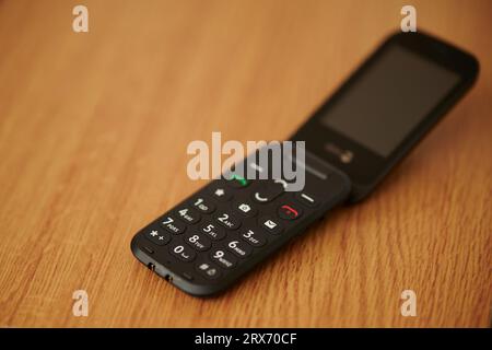 16 Sep 2023 - England  UK : Old style dumb mobile phone clam phone on wooden table Stock Photo