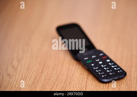 16 Sep 2023 - England  UK : Old style dumb mobile phone clam phone on wooden table Stock Photo