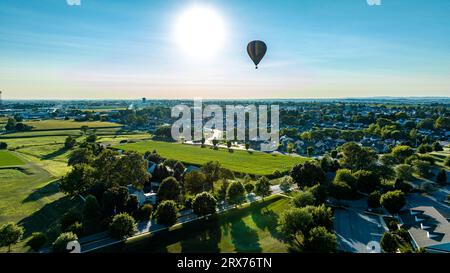 An Aerial View on a Striped Hot Air Balloon Floating Over a Countryside Community, on a Late Afternoon, Beautiful Summer Day Stock Photo
