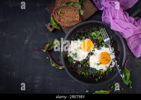 Breakfast. Fried eggs with green beet leaves, garlic, pepper and green onion in pan. Top view, flat lay Stock Photo