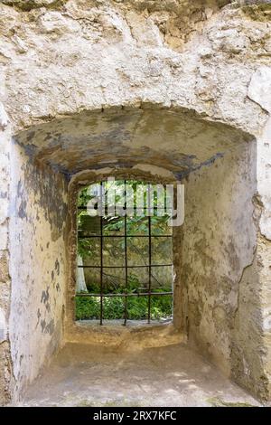 Window with lattice in stonework of old building. One arched window with metal bars on wall of aged house. Copy space. Selective focus. Stock Photo