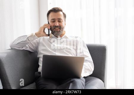 Happy senior manager business man relax at office sofa calling with friend while using laptop comfortable success people lifestyle Stock Photo