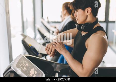 People running on a treadmill in health club using Smart Watch tracking pulse and training time for health goal Stock Photo