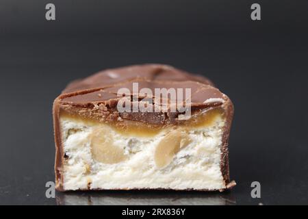 Chocolate candy bar cut with white nougat, nuts, peanuts and caramel in milk chocolate. Day of chocolate sweets on a black background. Close-up food Stock Photo