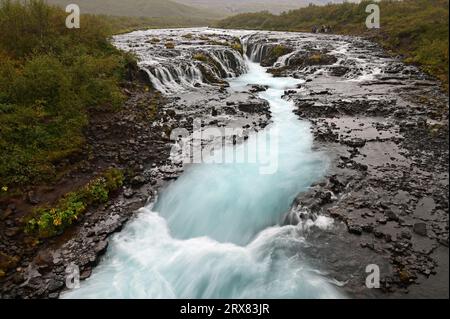 Distant tourists at Bruarfoss - Bridge Falls - on Iceland's Golden Circle route under cloudy autumn sky. Stock Photo