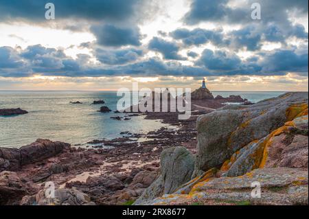 Road to La Corbiere lighthouse on the sea bottom in a low tide with cliff and sunset,  bailiwick of Jersey, Channel Islands, Great Britain Stock Photo