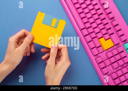 Hand holding floppy disk on color keyboard background, technology concept. High quality photo Stock Photo