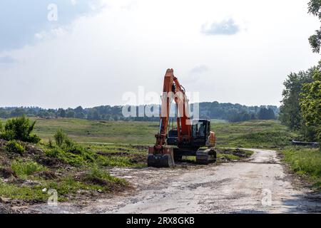 Orange excavator on dirt road - rural scenery with grassy field and trees Stock Photo