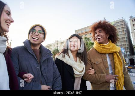 Multiracial colleagues strolling around the city hugging on a winter day. Couples fun outdoors.  Stock Photo